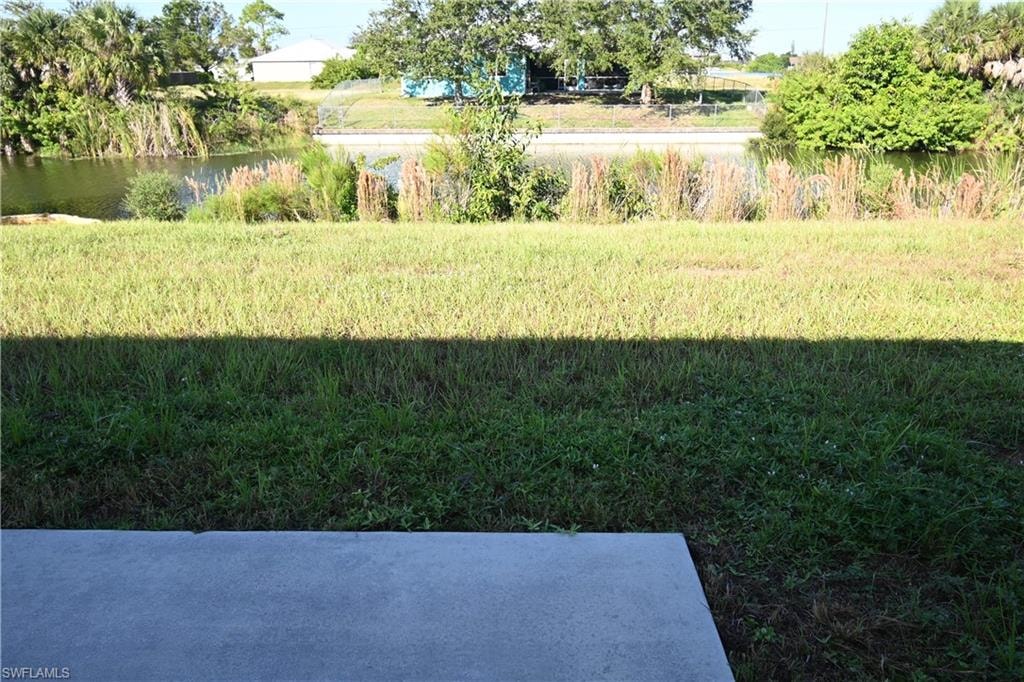 Concrete patio with a grass yard leading to a tranquil water feature surrounded by natural vegetation