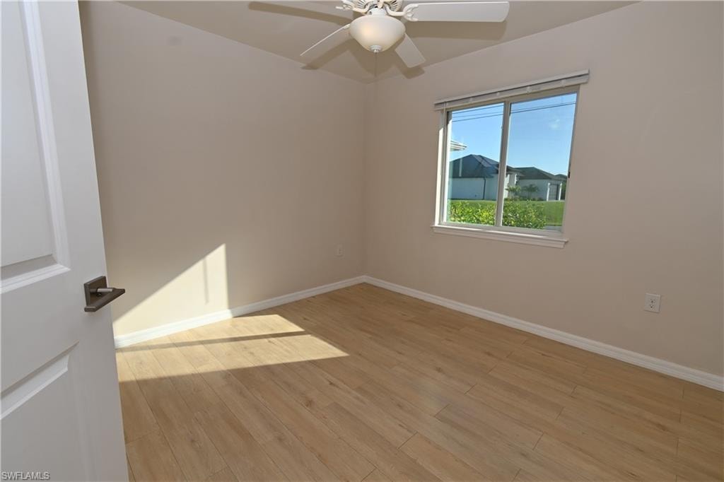 Wood-finish flooring, ceiling fan with light fixture, and a window with a white frame