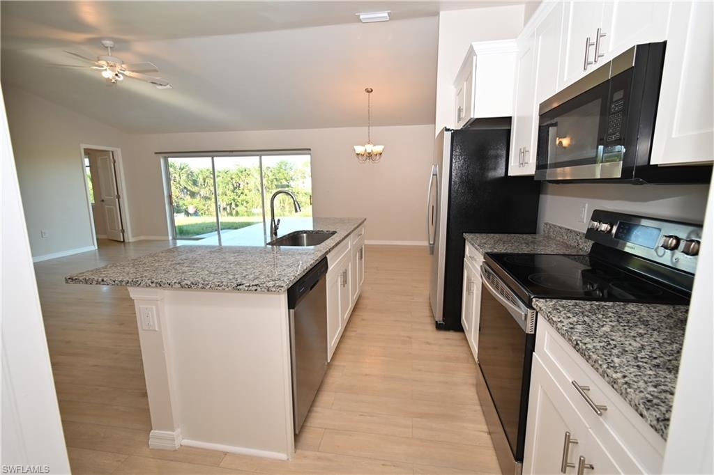 Kitchen featuring white cabinetry, granite countertops, stainless steel appliances, and a central island with an undermount sink
