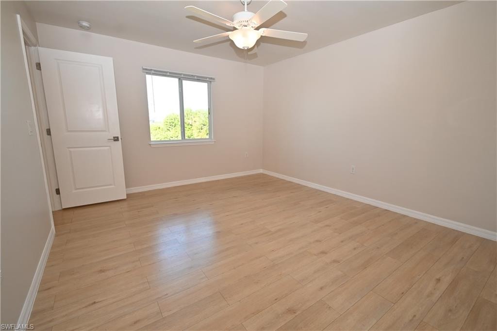 Wood-finish flooring, ceiling fan with integrated lighting, modern white door, and a sliding window
