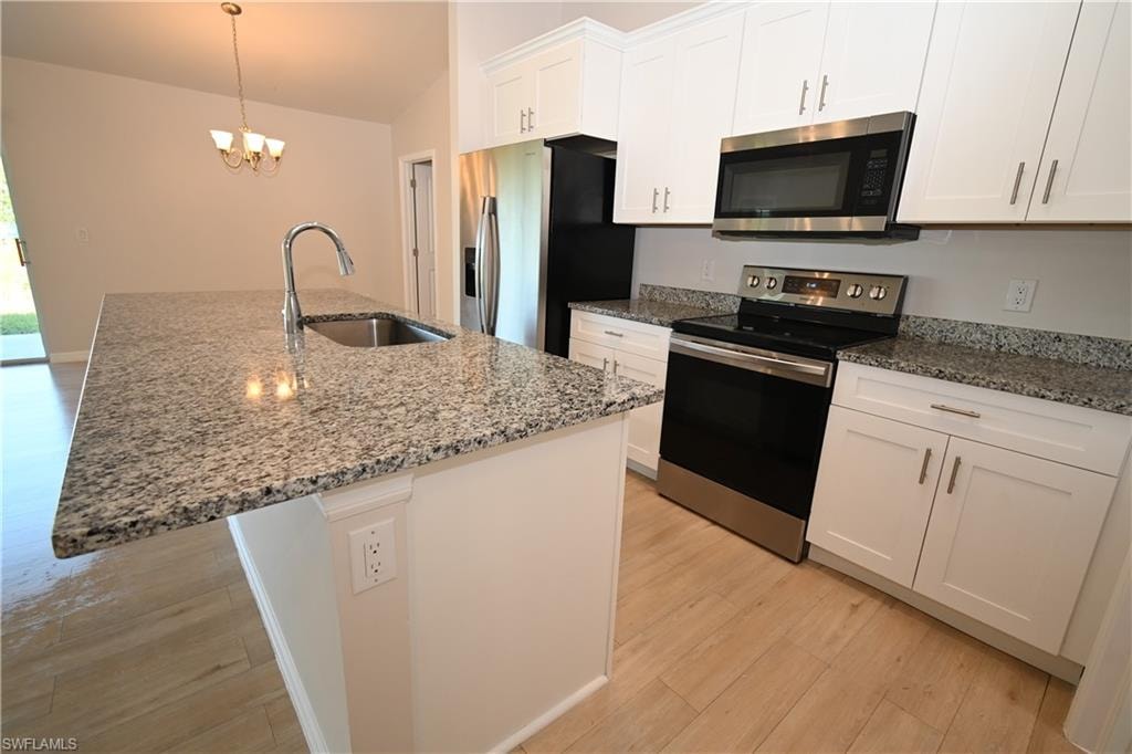 Kitchen featuring an island with an integrated sink and gooseneck faucet, light-toned wood-finish flooring, white cabinetry, granite countertops, and stainless steel appliances including a range and microwave