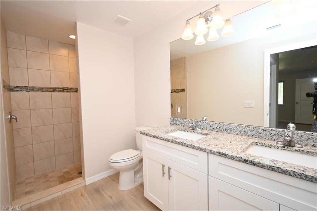 Walk-in shower with tiled surround and decorative accent band, dual white vanities with granite countertops, and wood-finish flooring