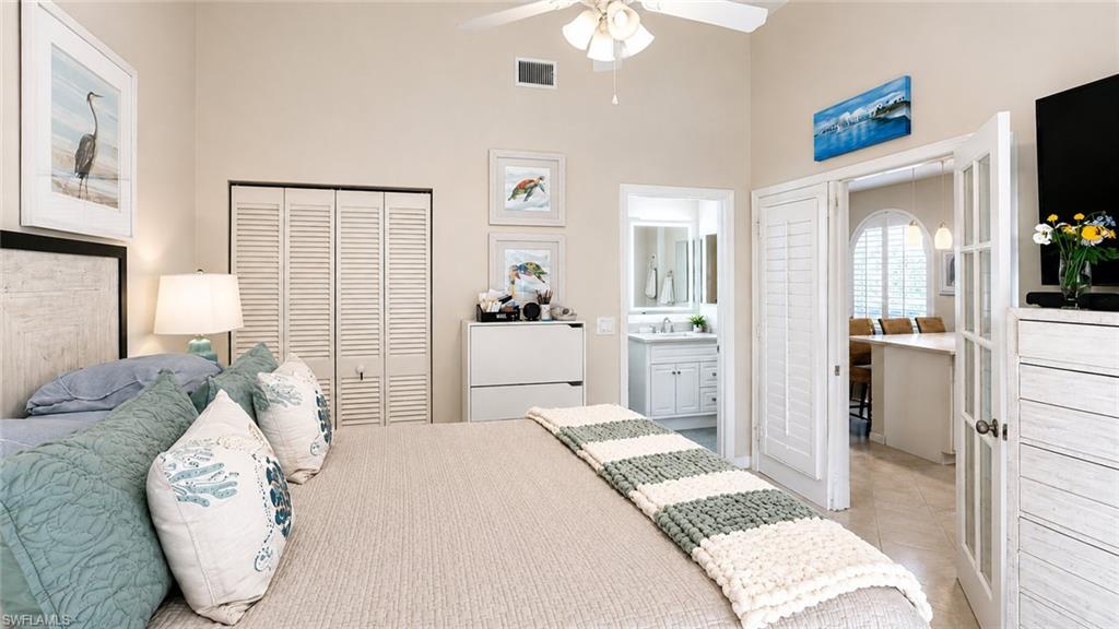 Spacious primary bedroom suite featuring warm neutral walls, ceiling fan, wood-finish flooring, and an ensuite bathroom with vanity and mirror