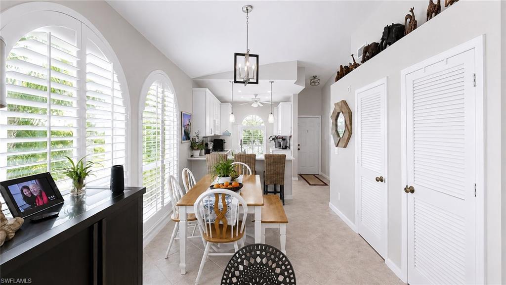Open-concept living area featuring a kitchen island with sink, white shaker cabinetry, tile backsplash, and a dining area with arched windows