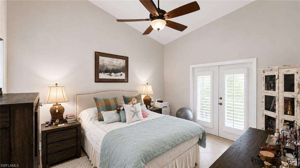 Vaulted ceilings featuring a ceiling fan, double French doors with plantation shutters, tile flooring, and a wood-finish dresser