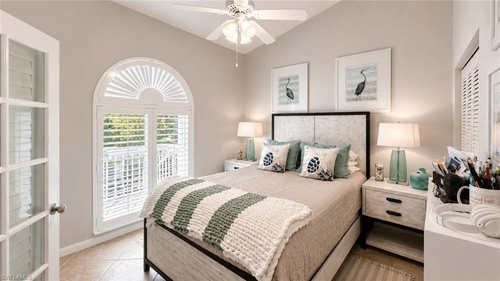 Vaulted ceiling with a ceiling fan, arched window with plantation shutters, French doors, and tile flooring