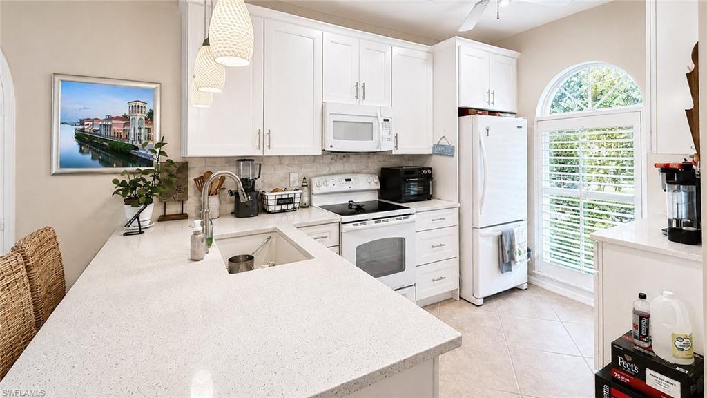 Kitchen featuring white cabinetry, light-toned countertops, a built-in kitchen sink, and a white appliance suite
