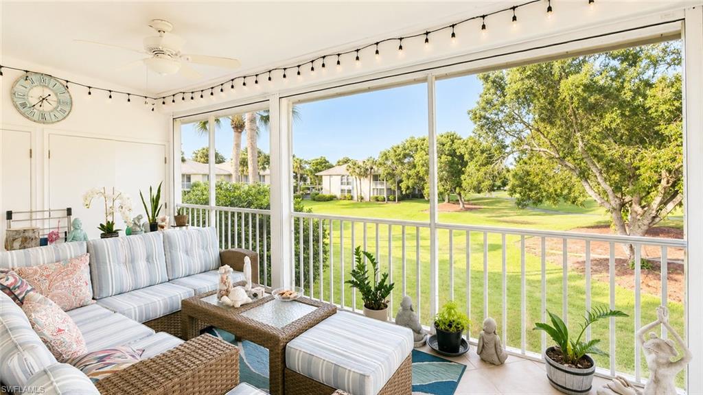 Screened-in porch featuring a ceiling fan, string lights, and white railings overlooking a green landscape with trees