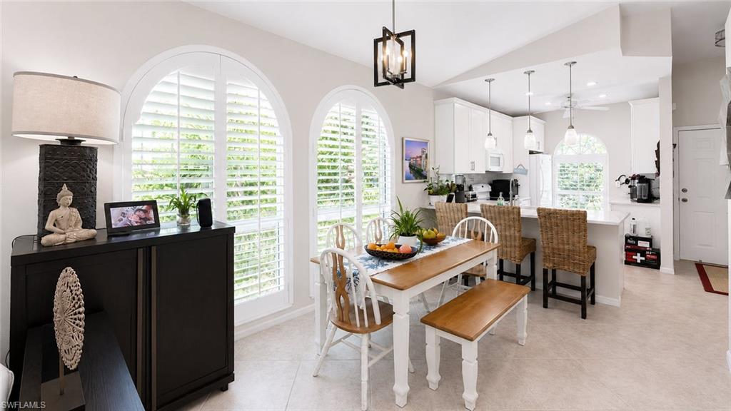 Arched windows with plantation shutters, kitchen with white cabinetry, ceiling fan, pendant lighting, and tiled flooring