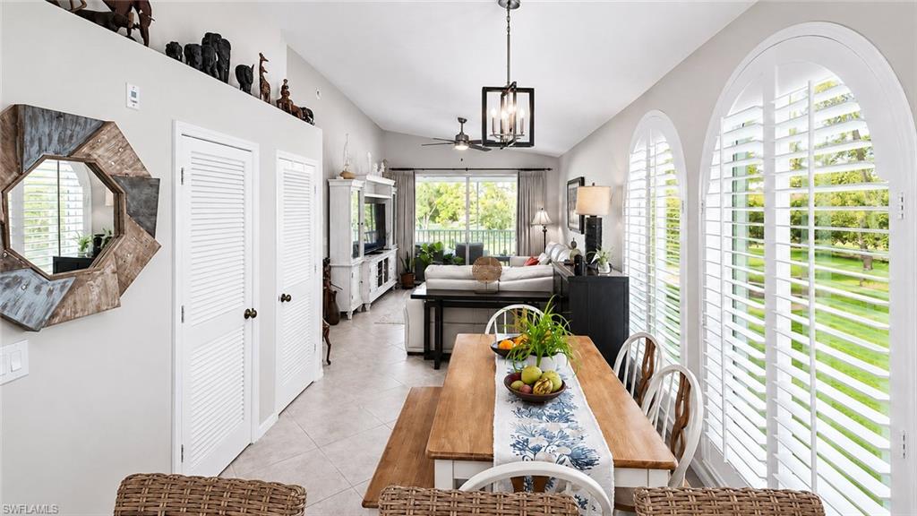 Tile flooring extending through an open-concept living and dining area, featuring two arched windows with plantation shutters, a vaulted ceiling, and a screened-in balcony