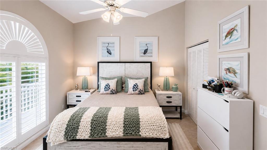 Vaulted ceiling with ceiling fan, louvered bi-fold closet doors, French doors, arched window with plantation shutters, and a vanity with a white cabinet and countertop