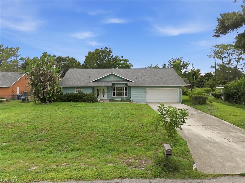 Single-story residence featuring a light blue exterior, a gray shingle roof, a two-car garage with a white door, a front lawn, and a paved driveway