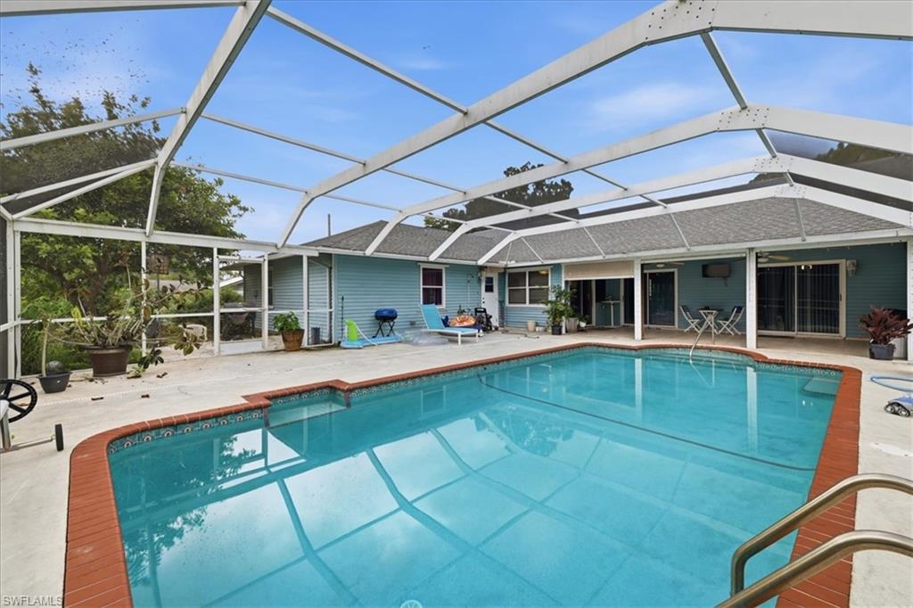 Screened swimming pool with a brick coping, concrete deck, and house exterior featuring blue siding