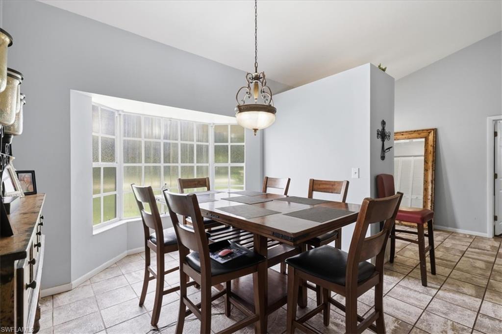 Dining area featuring a vaulted ceiling with an overhead light fixture, a bay window, and tile flooring