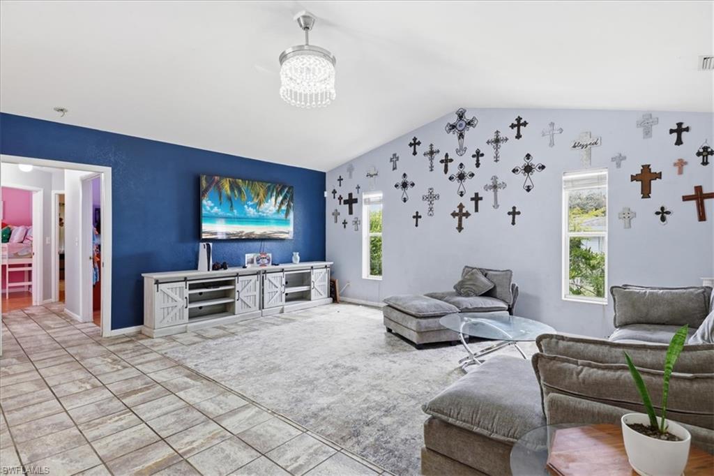 Vaulted ceilings highlight this expansive living area, featuring a decorative chandelier and a prominent accent wall
