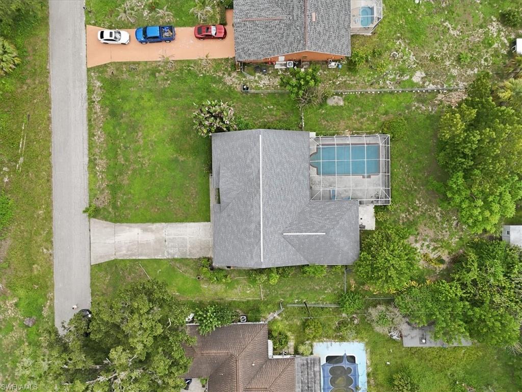 Aerial perspective showcasing a property with a grey shingle roof, a screened-in swimming pool, and a concrete driveway