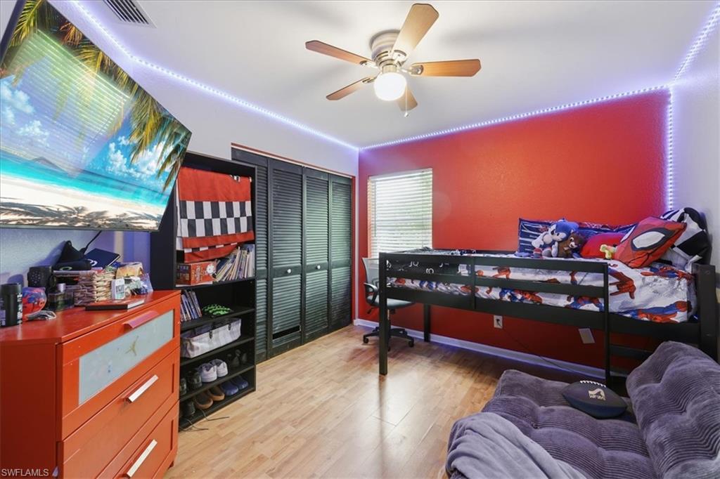 Room featuring wood-finish flooring, a ceiling fan with integrated lighting, and a window with horizontal blinds