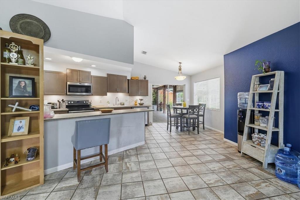 Open-concept kitchen and dining area featuring vaulted ceilings, light-toned cabinetry, and stainless steel appliances