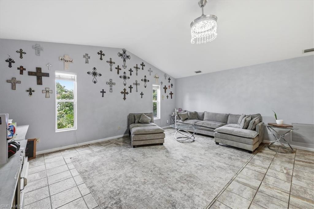 Spacious living area featuring vaulted ceilings, light tile flooring, and a crystal chandelier fixture