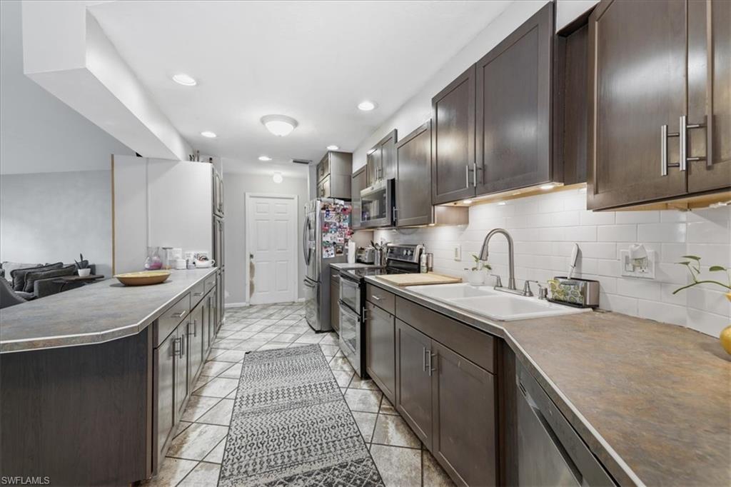 Galley kitchen featuring dark wood cabinetry, stainless steel appliances, a white subway tile backsplash, and recessed lighting