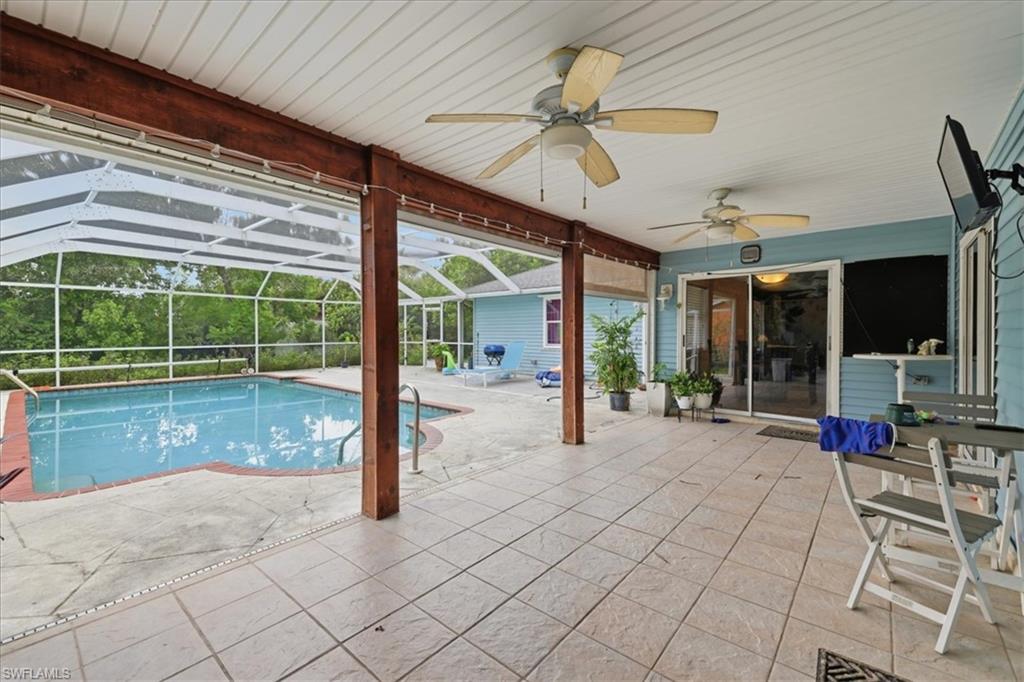 Covered patio with square tile flooring, wood-finish support beams, multiple ceiling fans, and a screened swimming pool with a concrete deck and brick coping