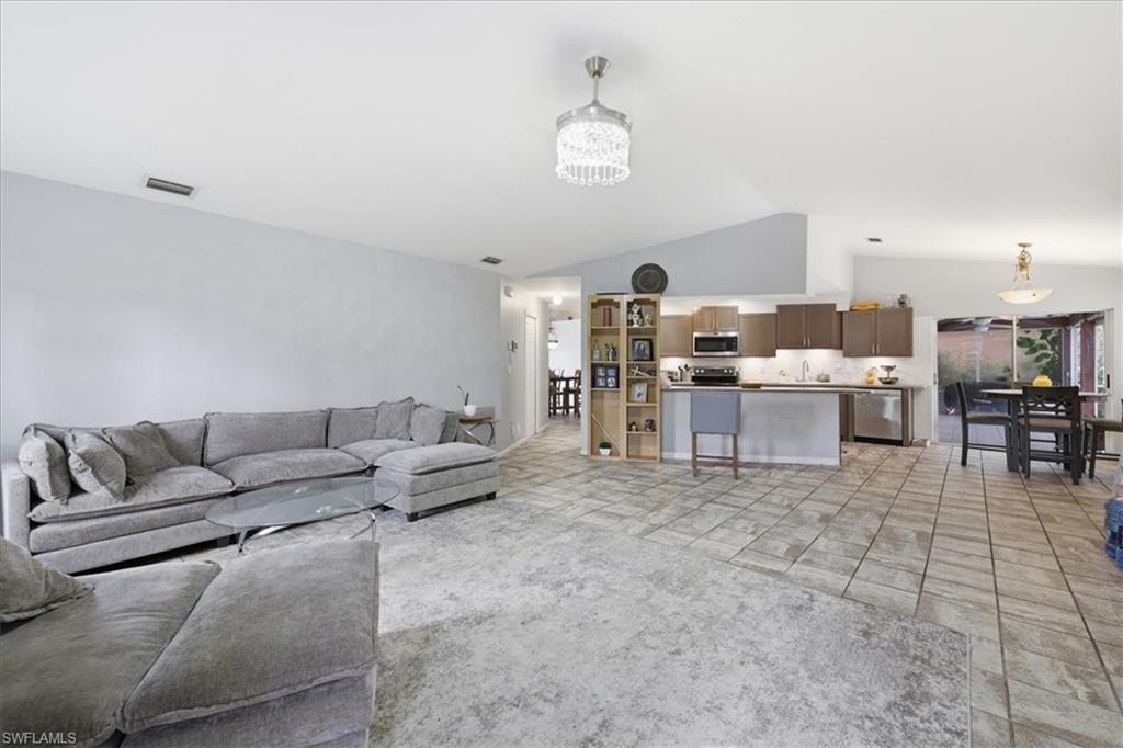 Expansive living area featuring vaulted ceilings, a contemporary chandelier, and a combination of carpet and tile flooring