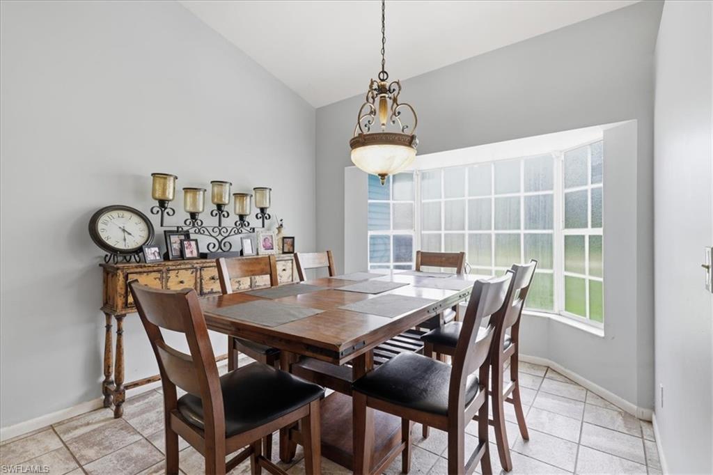 Vaulted ceiling dining area featuring a prominent bay window, overhead chandelier, and tile flooring