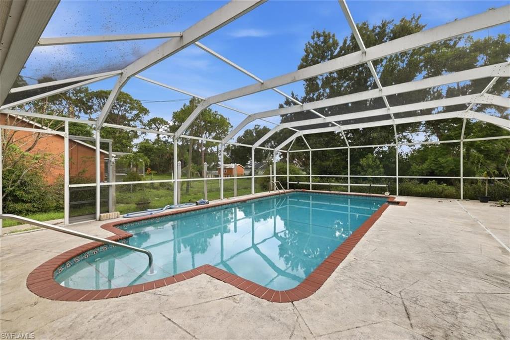 Screened swimming pool enclosure featuring a concrete deck, curved brick coping, and stainless steel handrail