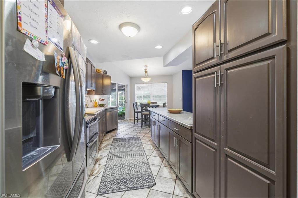 Galley kitchen featuring stainless steel appliances, dark wood-finish cabinetry, light-toned countertops, and tile flooring