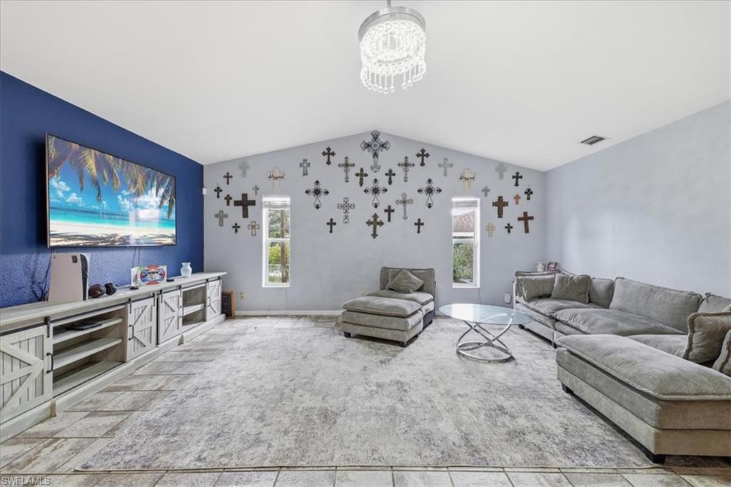 Vaulted ceiling living area featuring a decorative ceiling light fixture, accent wall, and multiple windows