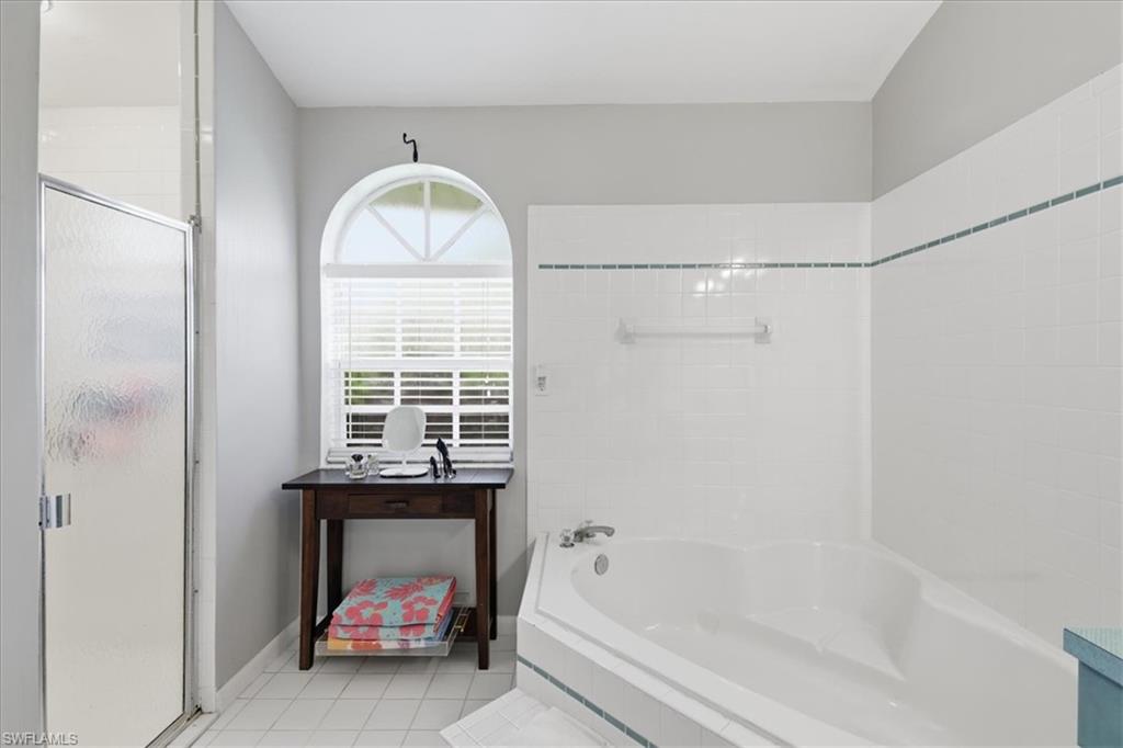 Bathroom featuring a corner soaking tub, a separate shower with a glass enclosure, and an arched window with blinds