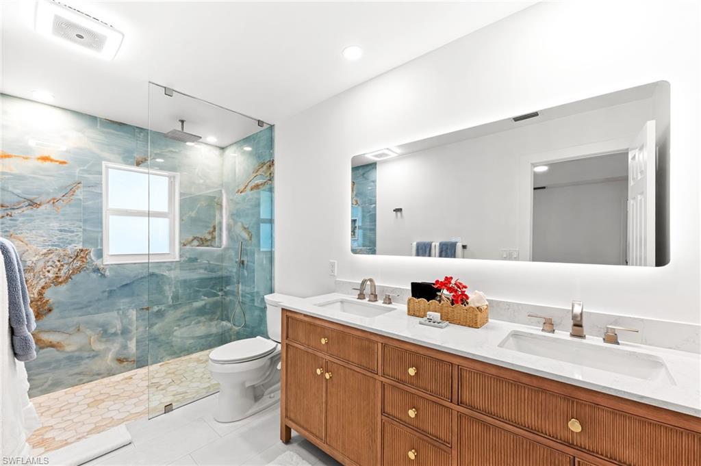Bathroom featuring double vanity, a marble finish shower, and light tile patterned floors