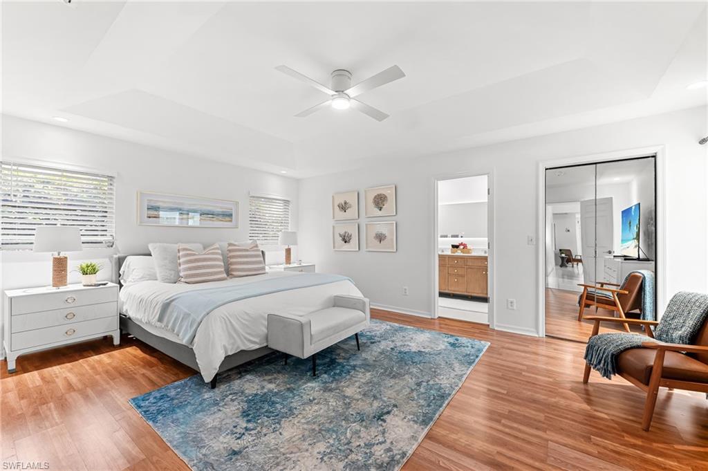 Bedroom featuring a tray ceiling, recessed lighting, light wood-type flooring, a ceiling fan, and connected bathroom