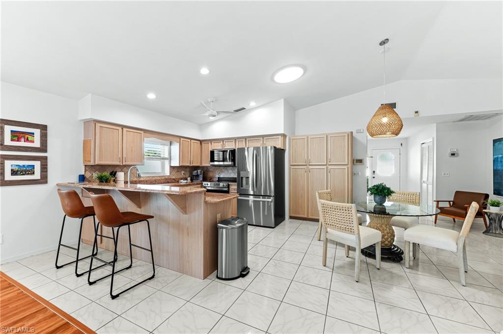 Kitchen with a kitchen bar, a peninsula, appliances with stainless steel finishes, vaulted ceiling, and decorative light fixtures