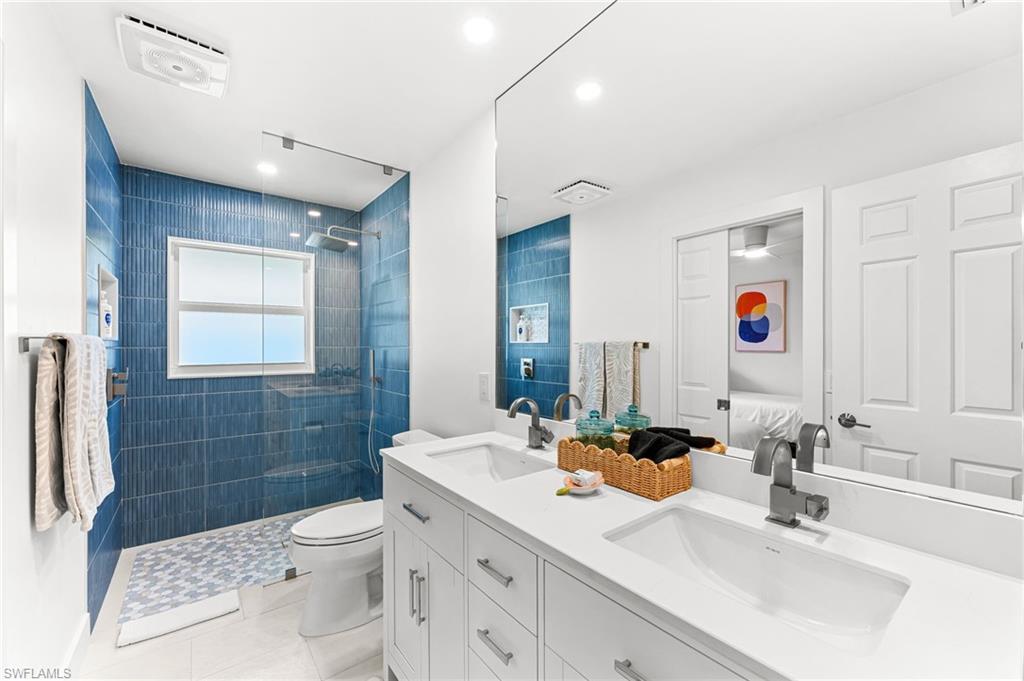 Ensuite bathroom with double vanity, a walk in shower, light tile patterned floors, and recessed lighting