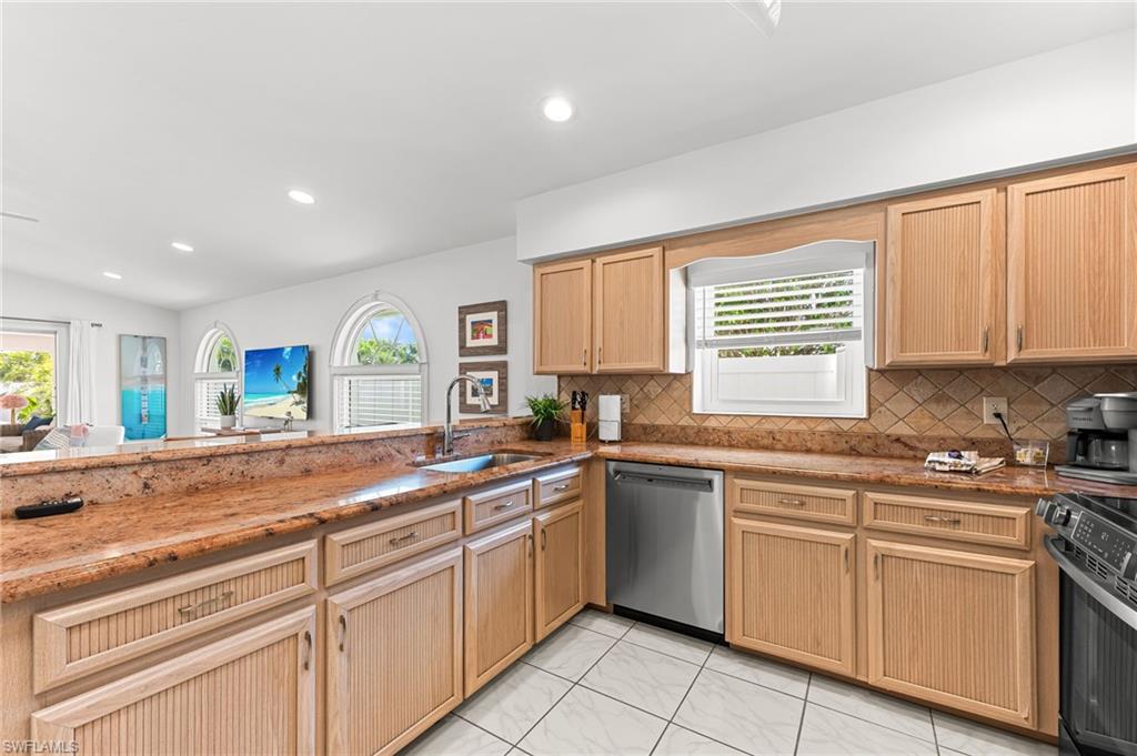 Kitchen with dark stone counters, dishwasher, decorative backsplash, black / electric stove, and light brown cabinets