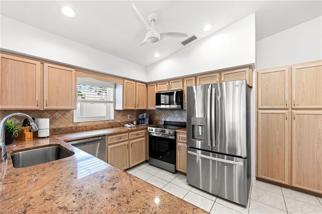 Kitchen featuring light brown cabinetry, appliances with stainless steel finishes, lofted ceiling, decorative backsplash, and a ceiling fan