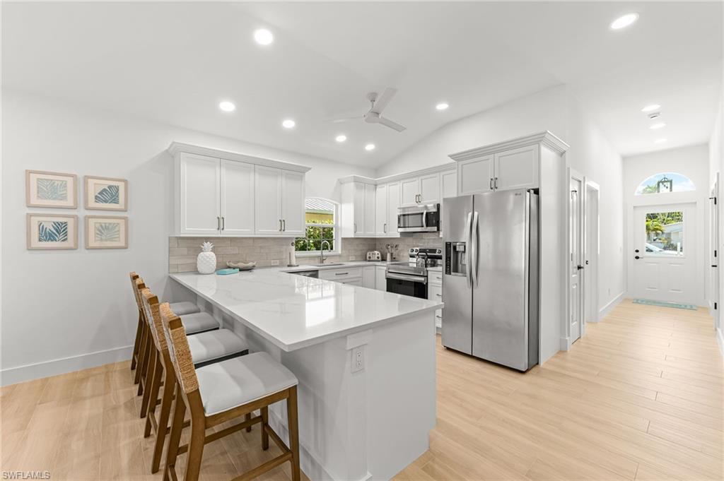 Kitchen with stainless steel appliances, white cabinetry, a peninsula, a breakfast bar area, and tasteful backsplash