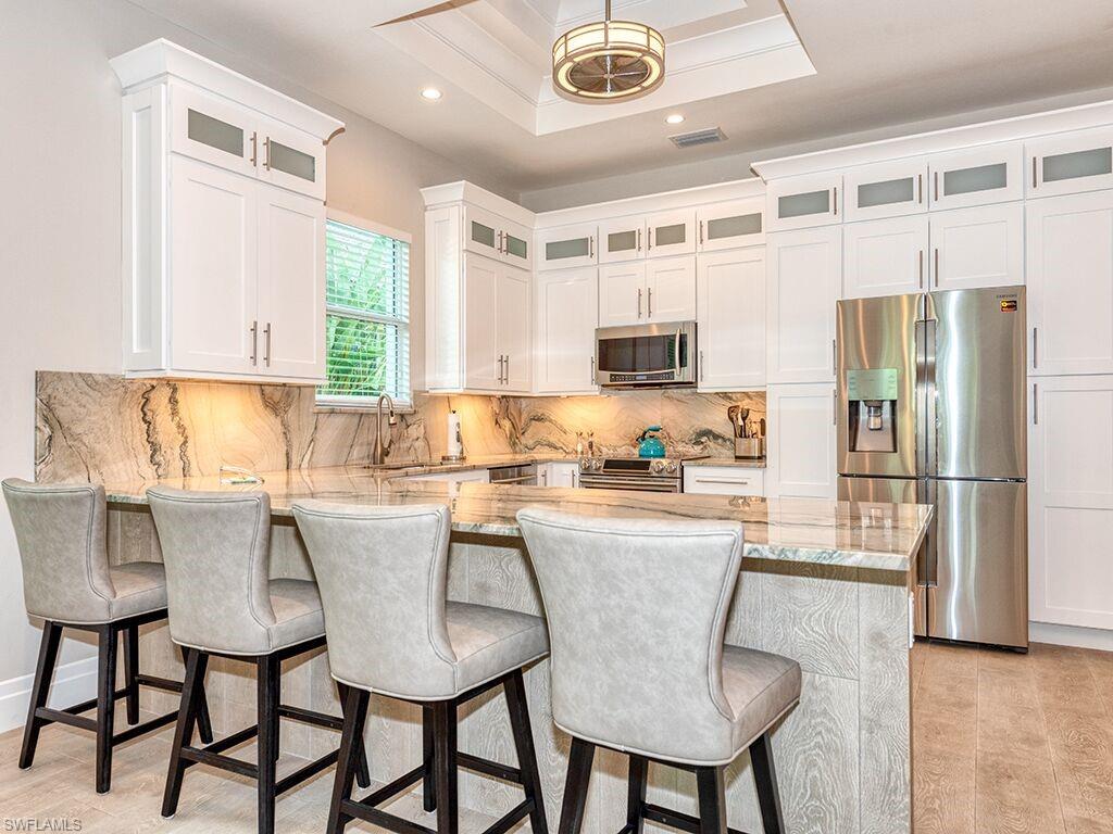 Kitchen featuring light stone countertops, stainless steel appliances, white cabinets, backsplash, and recessed lighting