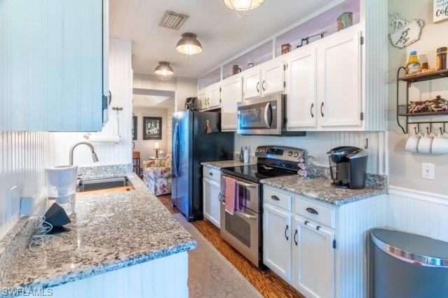 Granite countertops, white cabinetry, stainless steel appliances, beadboard paneling, wood-finish flooring