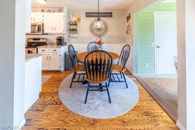Wood-finish flooring, white cabinetry, granite-style countertops, pendant lighting, and wainscoting