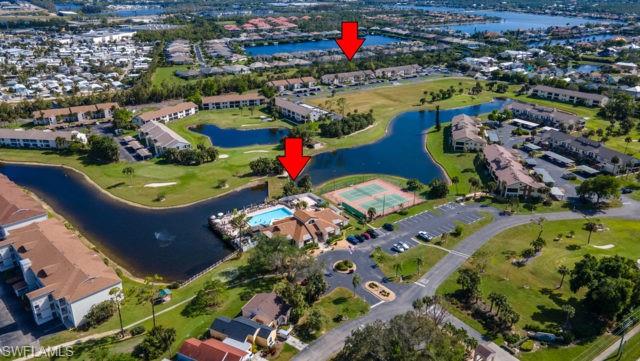 Community featuring multiple residential buildings, expansive green spaces, a large central pond, a pool area with a deck, and tennis courts