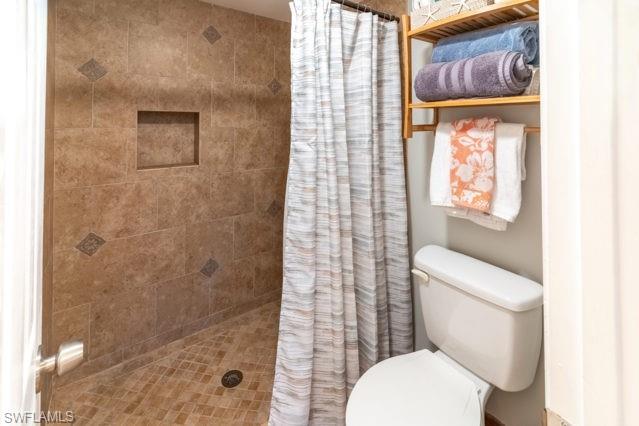 Tiled shower with an integrated niche and patterned accents, complemented by a white toilet and a built-in wooden shelving unit