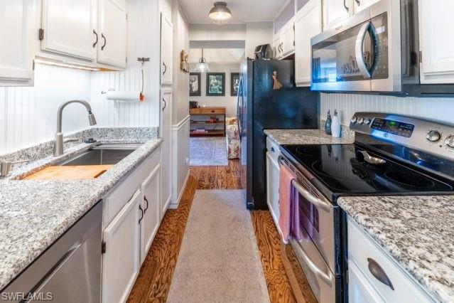Galley kitchen featuring wood-finish flooring, white cabinetry, granite countertops, and stainless steel appliances