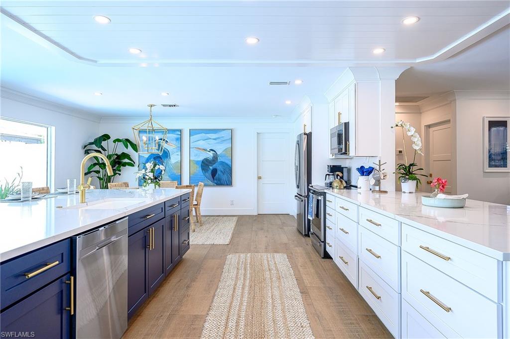 Kitchen with pendant lighting, light hardwood / wood-style floors, sink, white cabinets, and stainless steel appliances