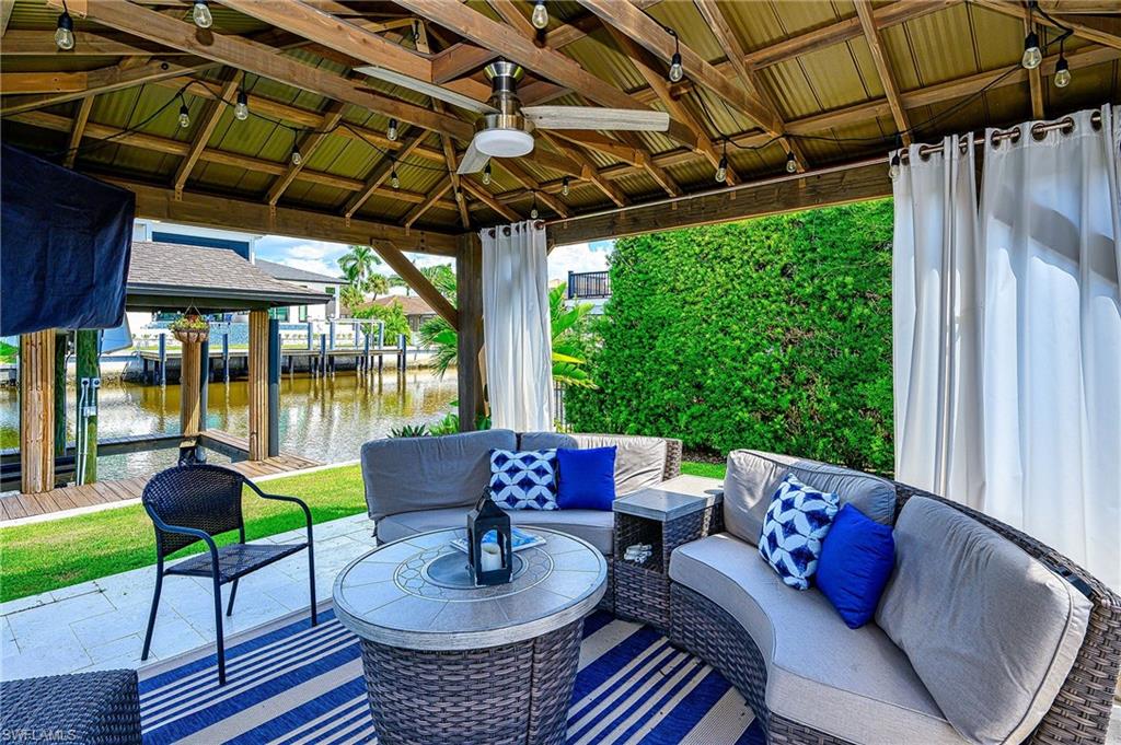 View of patio featuring ceiling fan, a boat dock, an outdoor hangout area, a gazebo, and a water view