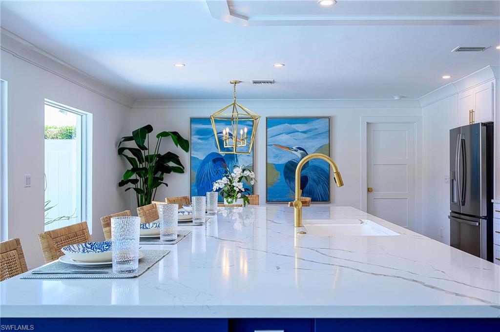 Kitchen with sink, a kitchen breakfast bar, decorative light fixtures, light stone countertops, and stainless steel fridge