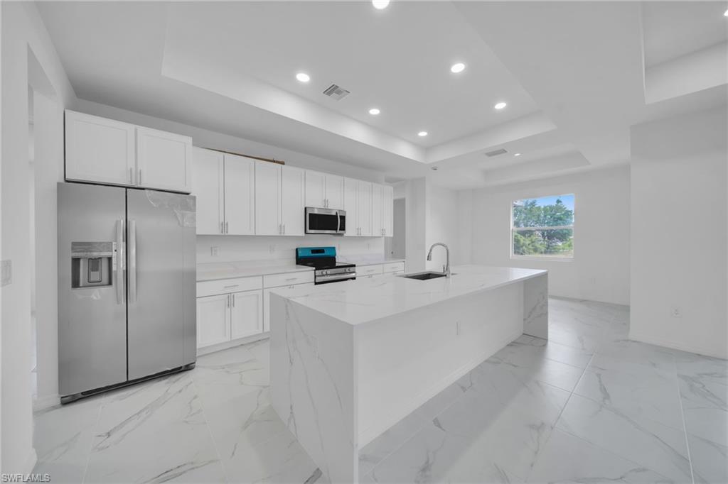 Contemporary kitchen showcasing white cabinetry, stainless steel side-by-side refrigerator with ice and water dispensers, and a large center island with waterfall-edge countertops