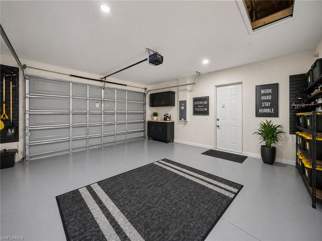 ai: example -Attached garage with an overhead door, smooth gray flooring, recessed lighting, and wall-mounted cabinetry