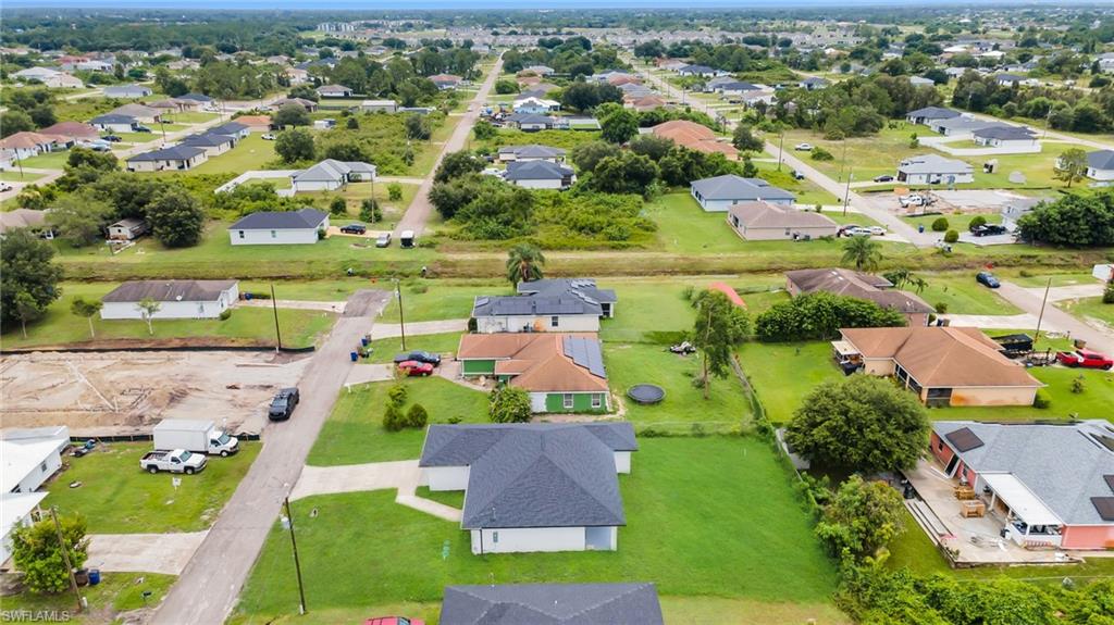Aerial view showcasing a modern residence featuring a dark-pitched roof and clean architectural lines, situated on an expansive manicured lawn with mature landscaping(ENHANCED GRASS COLOR FOR VISIBILITY PURPOSES)